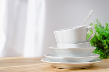 clean dishes - plate, saucer, cup, spoon, on white and green background on a wooden table
