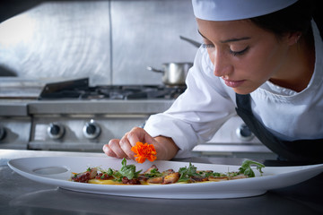 Chef woman garnishing flower in dish at kitchen