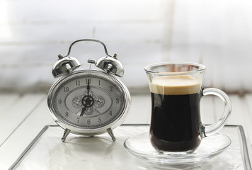 Alarm clock with cup of coffee and white background selective focus