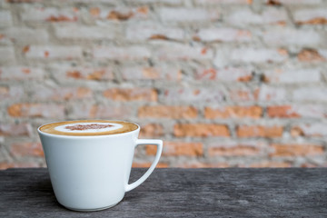 Cappuccino coffee in white cup on wooden table with old brick wall background