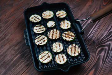 Zucchini grilled on a black pan. Dark wooden background.