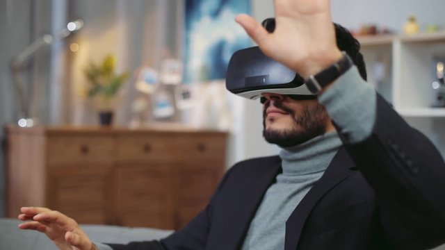 Handsome young man uses the virtual reality glasses, gestures actively. Gaming, modern users, having fun. Light, cozy living-room. Slow motion, camera stabilizer shot, male portrait
