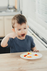 a child in the kitchen eats eggs or omelets in the afternoon