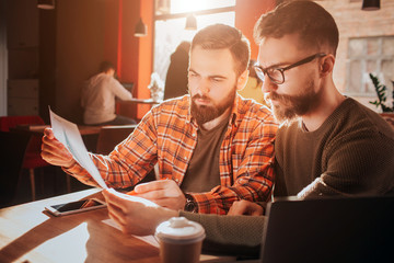 Close up of two hipsters-businessmen that looking to papers and learning information from them. They are preparing for business meeting. Cut view.
