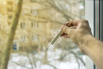 hand with a thermometer of a sick person at the window, bored on the street and fresh air. on a blurred background of the street and courtyard