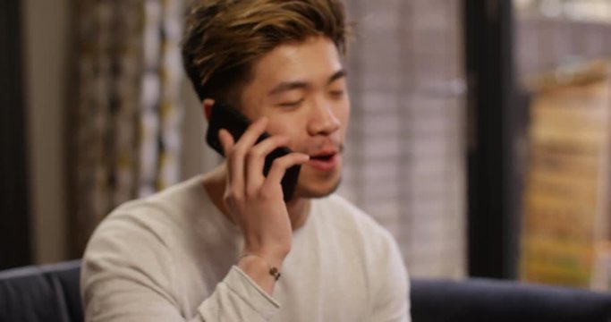 4K Cheerful Asian man talking on the phone at home. Slow motion.