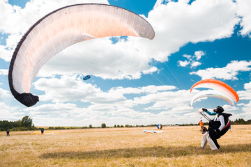 A man with a paraglider catches streams of wind on a yellow field against a blue sky on a summer...