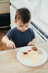 little baby boy in the kitchen eating pasta with cutlets, very tasty