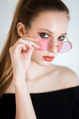 Sexy blonde woman in pink glasses on white background. Beautiful girl with professional makeup looking at the camera