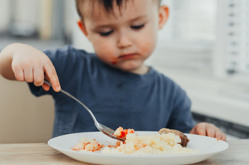 little baby boy in the kitchen eating pasta with cutlets, very tasty