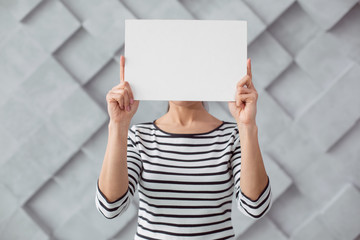 Read this. Nice pleasant young woman standing and covering her face while holding a sheet of paper