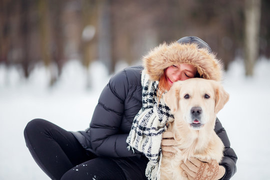 Photo of woman in black jacket squatting next to dog in winter park