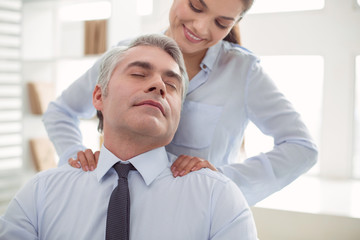 Absolutely relaxed. Pleasant nice adult man sitting in the chair and closing his eyes while receiving a massage
