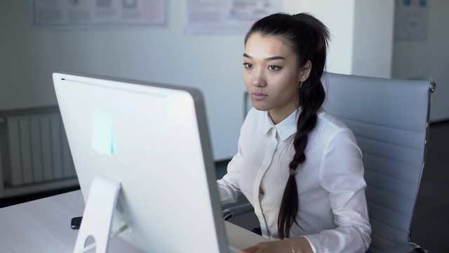Asian business woman is sitting on desk and starts working at computer in office. Concept: Asian woman, business office, work at computer