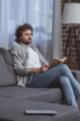 handsome man holding book with remote control on foreground