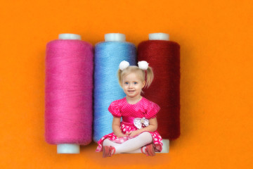 A little child in the world of big things. The girl in the red dress sits about three huge coils with sewing threads.