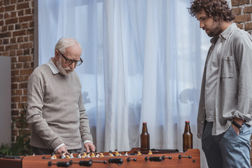 adult son and senior father playing table football with beer at home