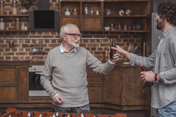 adult son giving senior father bottle of beer at home
