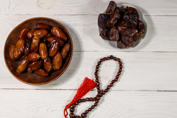 Dates fruit and rosary on white wooden table. Top view