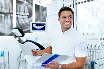 Handsome male dentist in doctors white lab coat posing in modern dental office