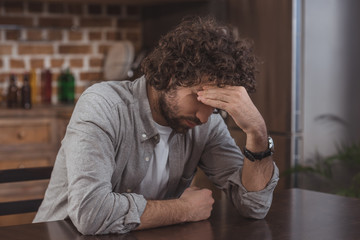 Obraz premium tired man sitting at table in kitchen and touching head