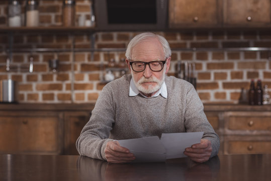 Handsome Grey Hair Man Sitting At Table And Looking At Photos At Home