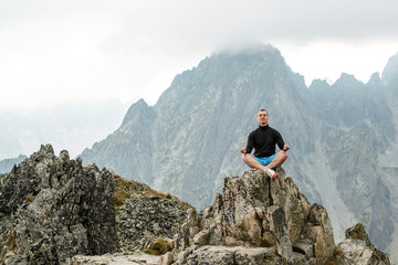 The young man sits on top of the mountain in Lotus pose.