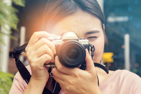 pretty cool young Asian woman with retro film camera or mirrorless camera in modern garden open mall.young woman holding mirrorless camera in vintage tone;
