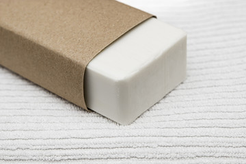 piece of white soap wrapped in a brown craft paper on a white towel background concept of body care