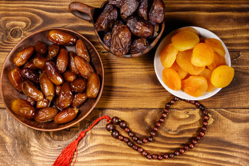 Dried apricots and dates fruit with wooden rosary on wooden table. Top view