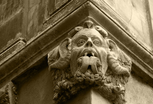 Gargoyle with protruding tongue. Architectural detail of old house in medieval town of  Arles. Provence, France. Sepia historic photo.