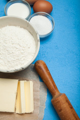Sweet baking - the ingredients of the dough recipe (eggs, flour, milk, butter, sugar) on a blue table. Background layout.