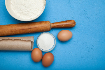Ingredients and cooking utensils for making a cake or dessert on a blue table.