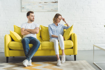 Upset couple sitting after argue on couch in front of wall with painting