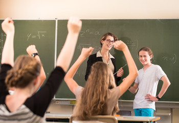 Lehrerin oder Dozent steht im Unterricht vor einer Tafel und unterrichtet Schüler, die sich melden...