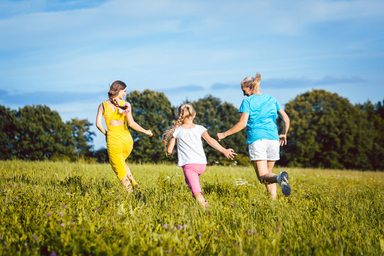 Zwei Frauen und ein Mädchen spielen auf einer Sommerwiese und laufen