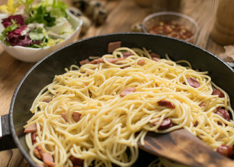 Spaghetti with sausages, cheese and quail eggs in a frying pan.