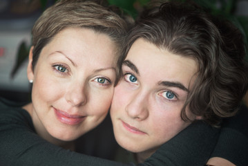 Happy young mom with short hair hugs her teenage son and smiles. A boy looks sad eyes.