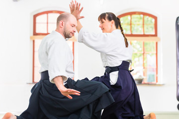 Man and woman fighting at Aikido training in martial arts school 