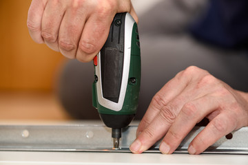 Close up on hands with cordless screwdriver assembling furniture