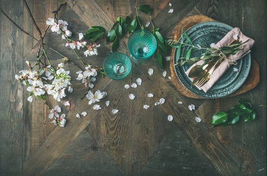 Flat-lay of Spring Easter holiday Table setting. Tender almond blossom flowers on branches, plates, glasses and cutlery over vintage wooden table background, top view, copy space