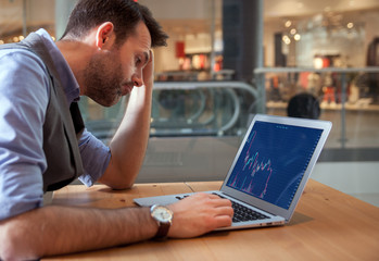 Depressed investor analyzing crisis stock market with charts on screen at restaurant