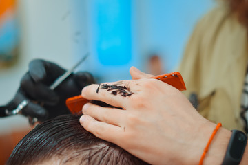 Brunette man getting a haircut by a professional hairdresser using comb and grooming scissors. Closeup view with shallow depth of field.