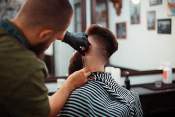 Handsome bearded man is getting shaved by hairdresser at the barbershop