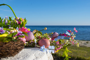 colorful easter eggs and branch with flowers by the sea