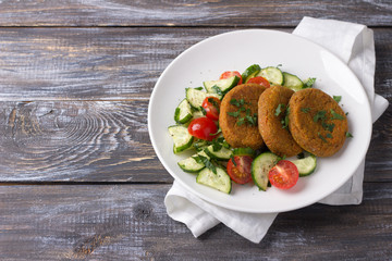 Carrot cutlets with amaranth, salad of fresh cucumbers and tomatoes on a wooden table, free space. Delicious healthy homemade food