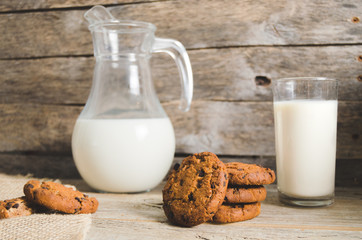 Oatmeal chocolate chip cookies, jug and glass of milk, rustic wooden background.