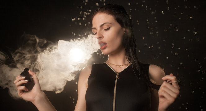 Young beautiful woman vaping e-cigarette in rain. Water flowing on woman face.