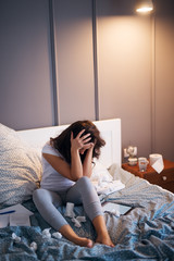 Naklejka premium Illness frustrated middle aged women sitting on the bed and holding tight her hair with both hands while trying to work on a tablet and papers at night.