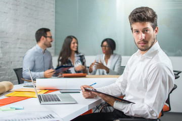 Handsome man in businesswear with clipboard and pen sitting near desk in workplace